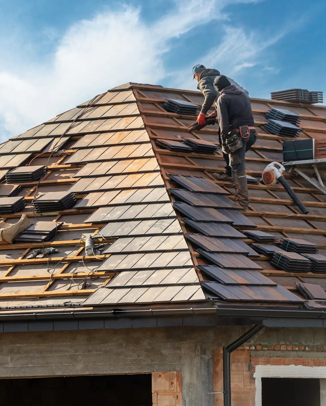 Roofing crew installing dark slate tiles on a residential roof