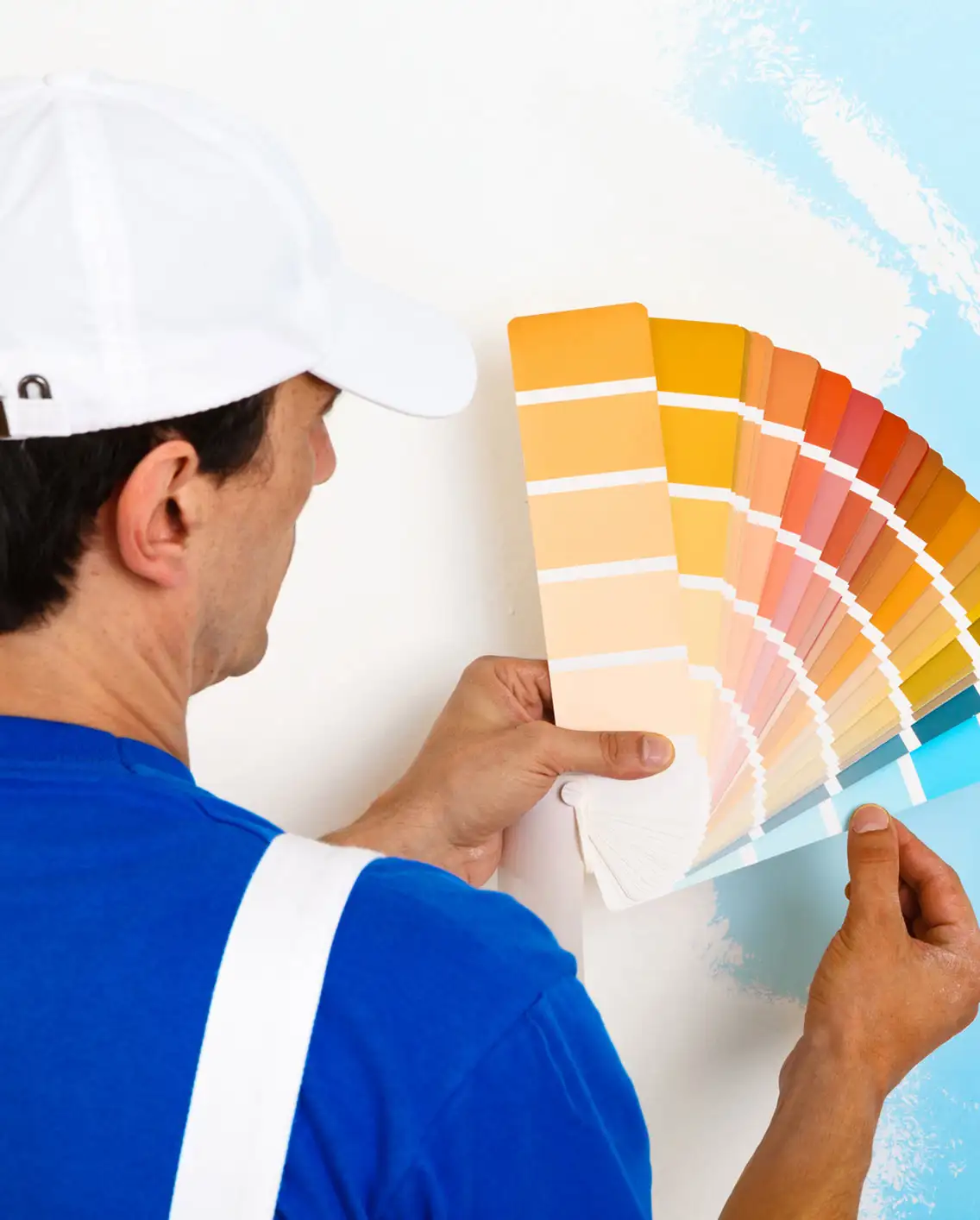 Painter comparing paint color swatches against a freshly painted wall