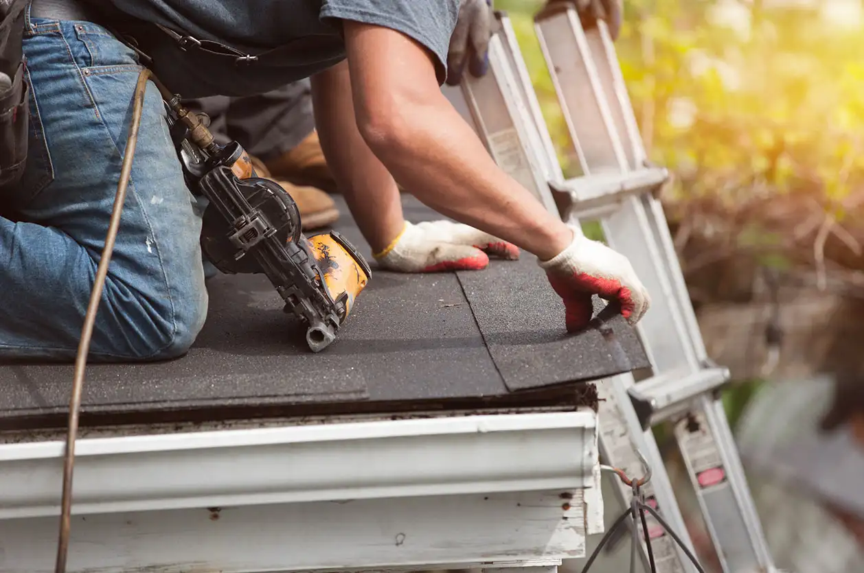 Roofer using a nail gun to install asphalt shingles on a sloped roof